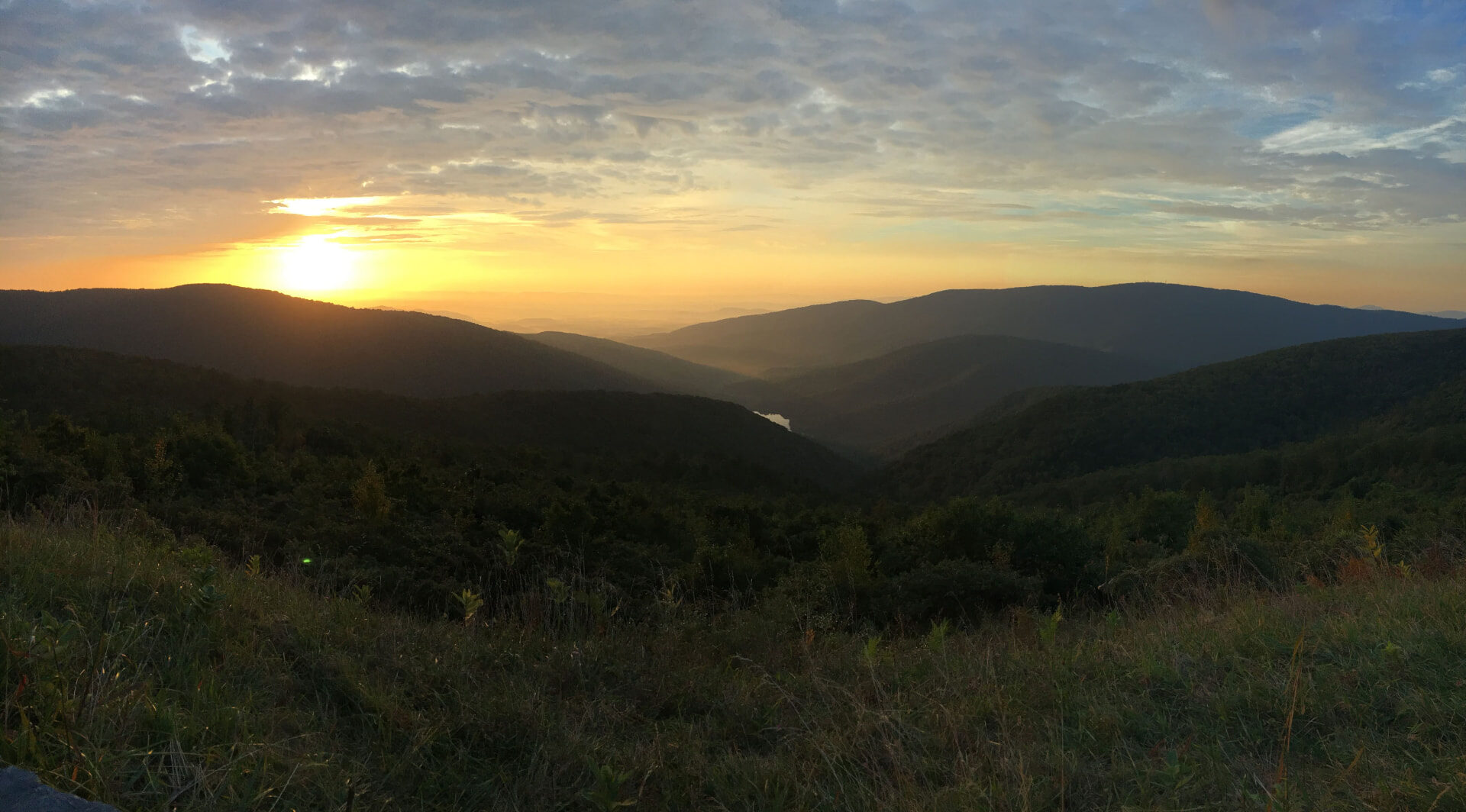 Sunrise over layered Blue Ridge mountain ridges and a meadow in the foreground